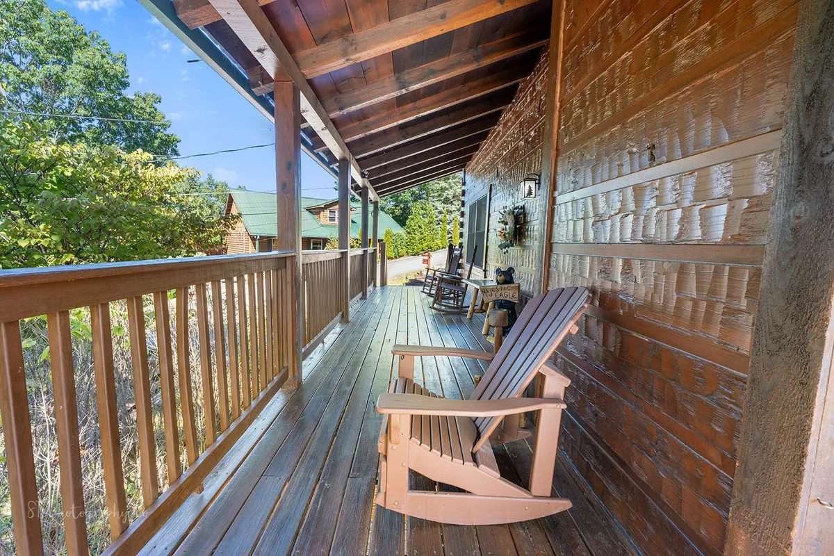 A spacious balcony with wooden rocking chairs overlooks natural greenery. The setting exudes tranquility and invites relaxation, whether it's sipping coffee on a crisp fall morning or unwinding after a day of activities. The porch feels like an extension of the home into the outdoors.