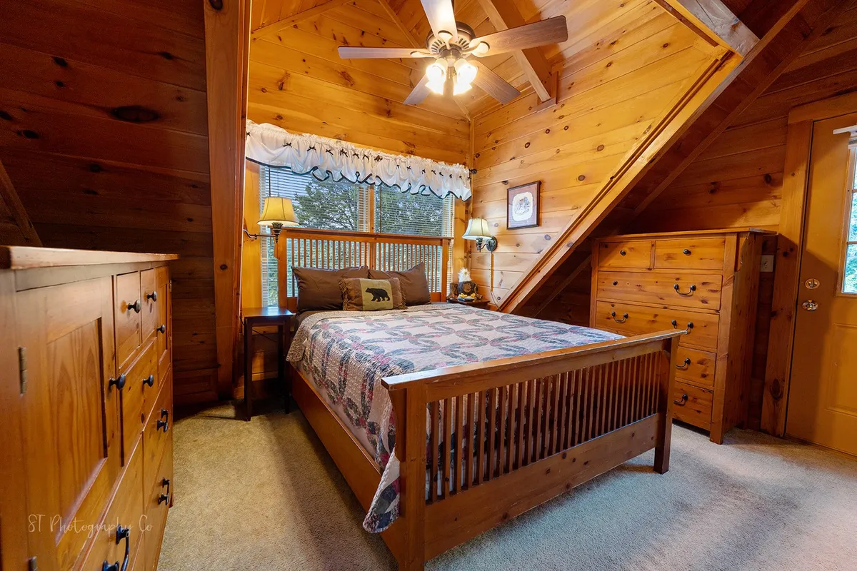 A warm and inviting bedroom featuring a wooden bed with decorative pillows, a chest of drawers, and a window with natural light filtering through curtains. The tranquil setting highlights a restful atmosphere ideal for recharging.