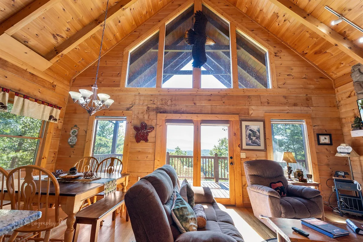 A welcoming interior shot showcasing a large wooden dining table set near expansive windows, comfortable seating nearby, and rustic wooden beams overhead. The natural light and scenic views create a warm, communal atmosphere.