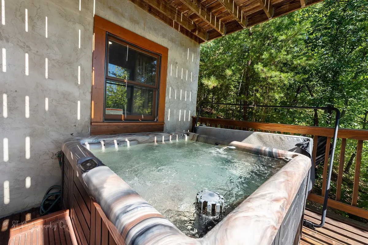 A tranquil outdoor hot tub situated on a wooden deck, surrounded by lush greenery. The inviting spa is perfectly positioned for soaking under the open sky and enjoying natural serenity, all just steps away from the cabin.