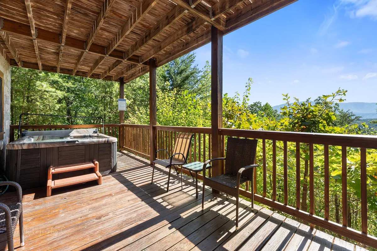 An inviting exterior shot of a wooden deck featuring a hot tub, surrounded by greenery and a sweeping mountain view. The scene is peaceful and beckons guests to unwind after a day outside in the national park.