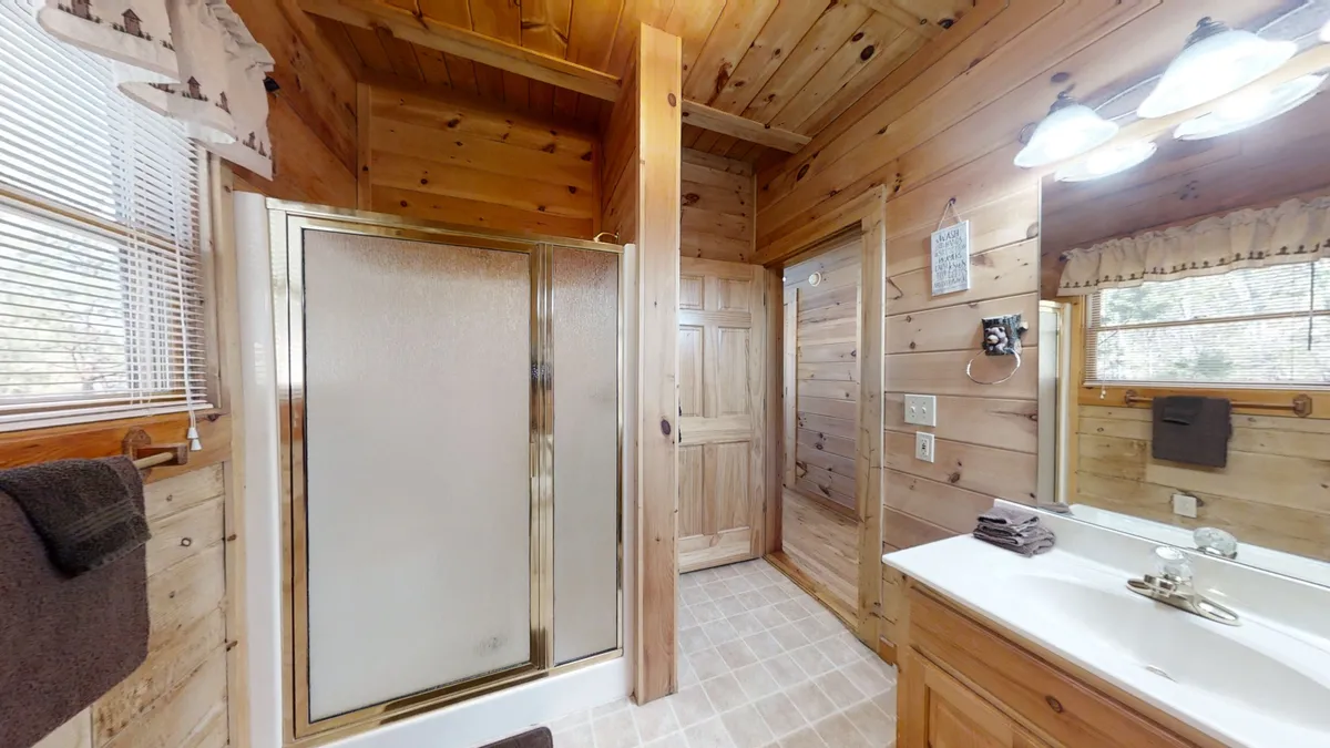 A tastefully decorated bathroom featuring a glass shower enclosure, wooden cabinets, and a sink area with a large mirror. The warm tones and inviting design offer a glimpse into the property’s private and convenient amenities.