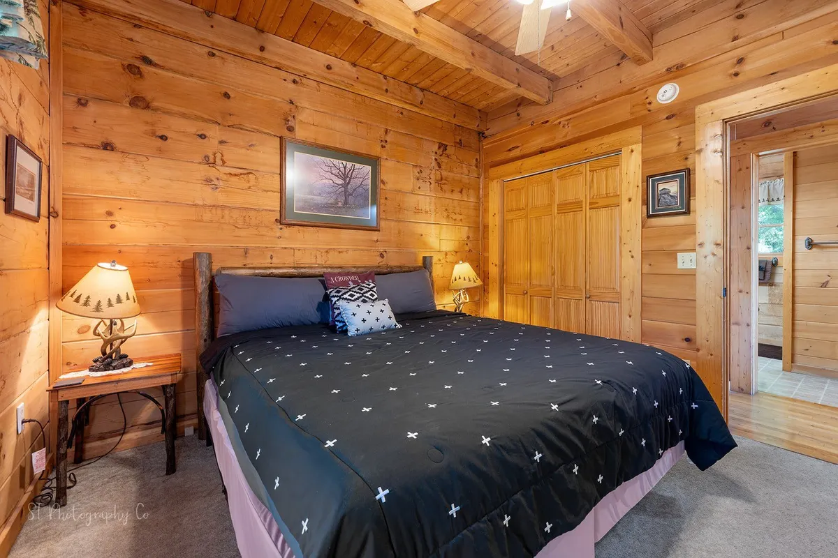 A relaxing bedroom with a patterned quilt on the bed, wooden wall paneling, bedside lamps, and framed artwork. The space feels intimate and cozy, ideal for quiet retreats or family stays.
