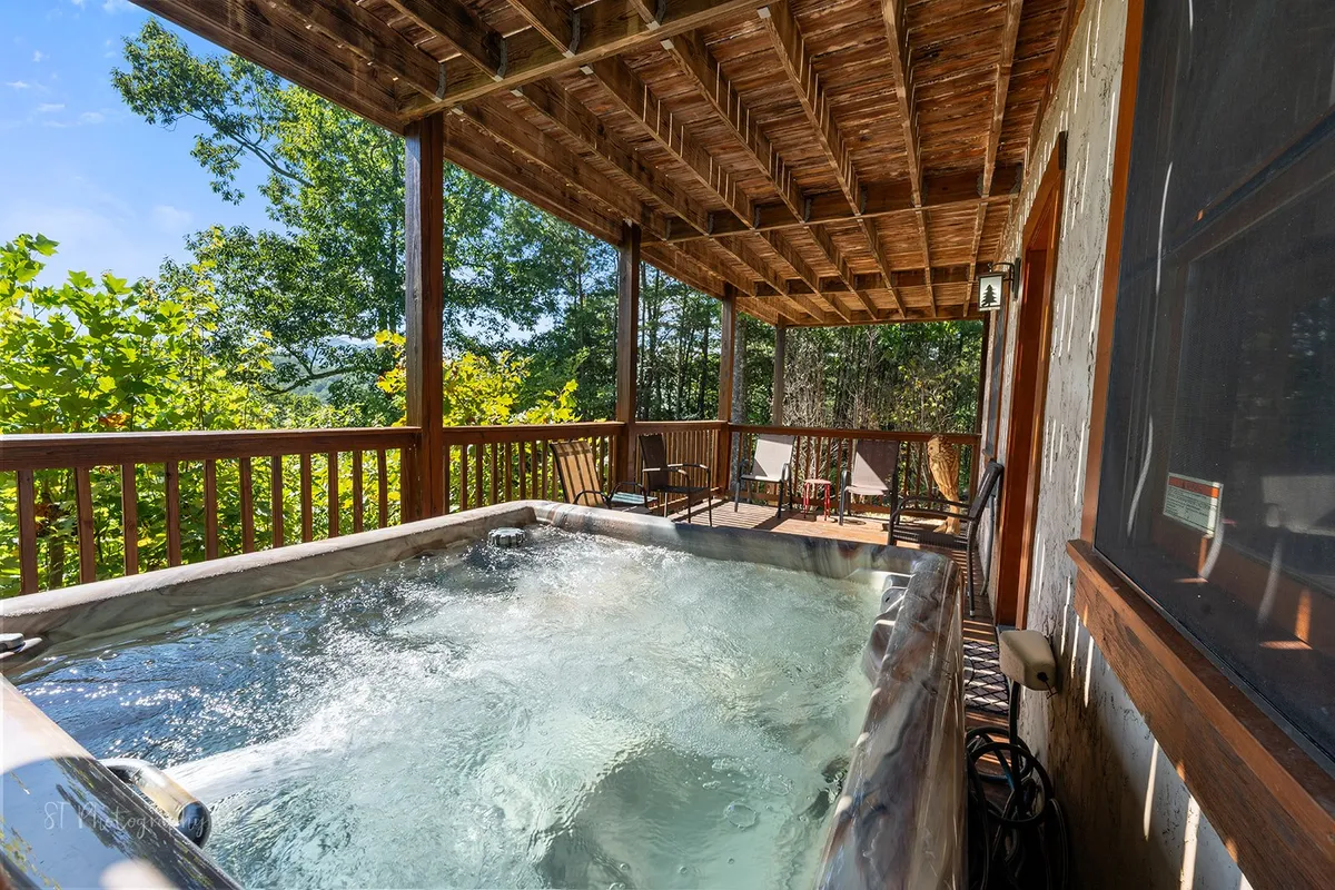 A bubbling hot tub sits on a private wooden deck surrounded by forest greenery. Lounge chairs are placed nearby, inviting relaxation, while the hot tub itself is perfectly positioned for sunset or starlit soaks. The deck’s secluded setting strengthens the sense of a private retreat amidst nature.