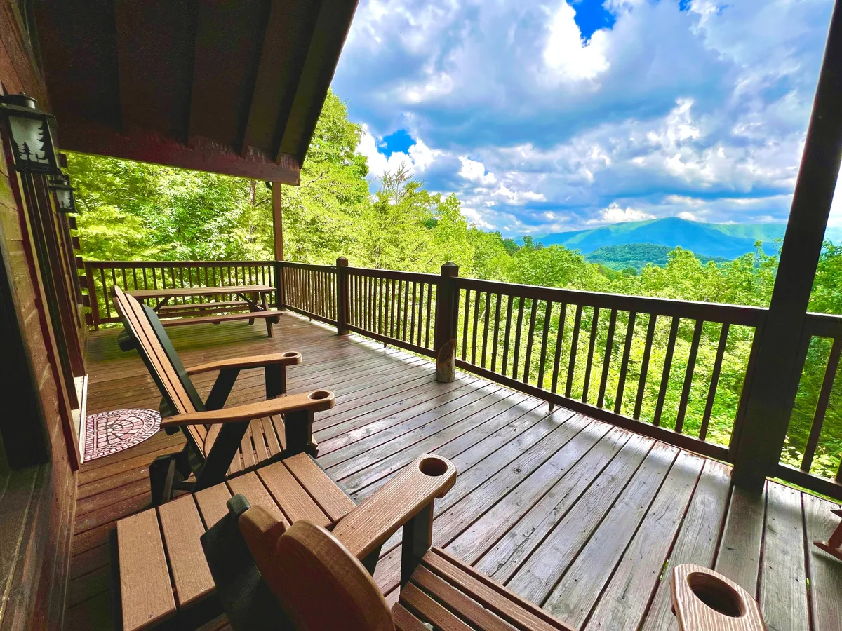 A wooden deck with two Adirondack chairs overlooks a sweeping view of the Smoky Mountains under a tranquil sky. The setting is peaceful, with the chairs positioned for enjoying sunrise coffee or evening wine while taking in the breathtaking mountain scenery.