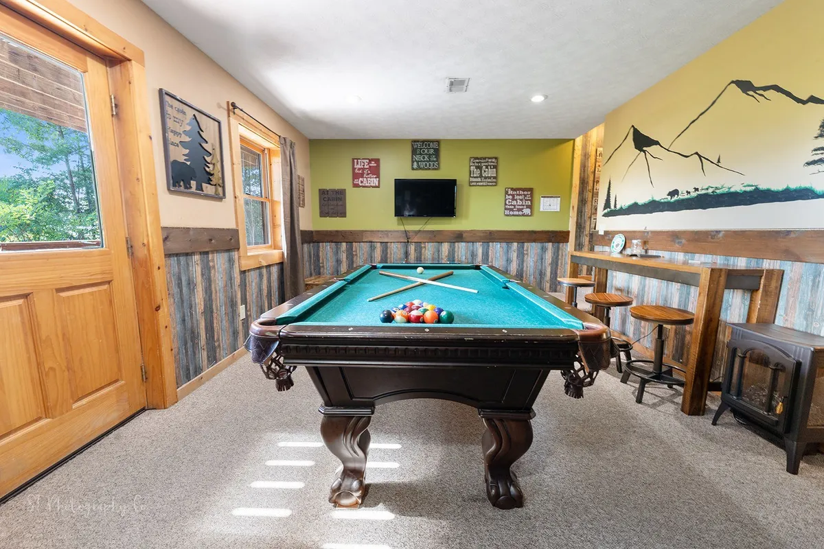 A spacious and stylish game room featuring a pool table as the centerpiece, with bar seating and decorative wall art adding to the playful, social atmosphere. The room is designed for friendly competitions and group gatherings.