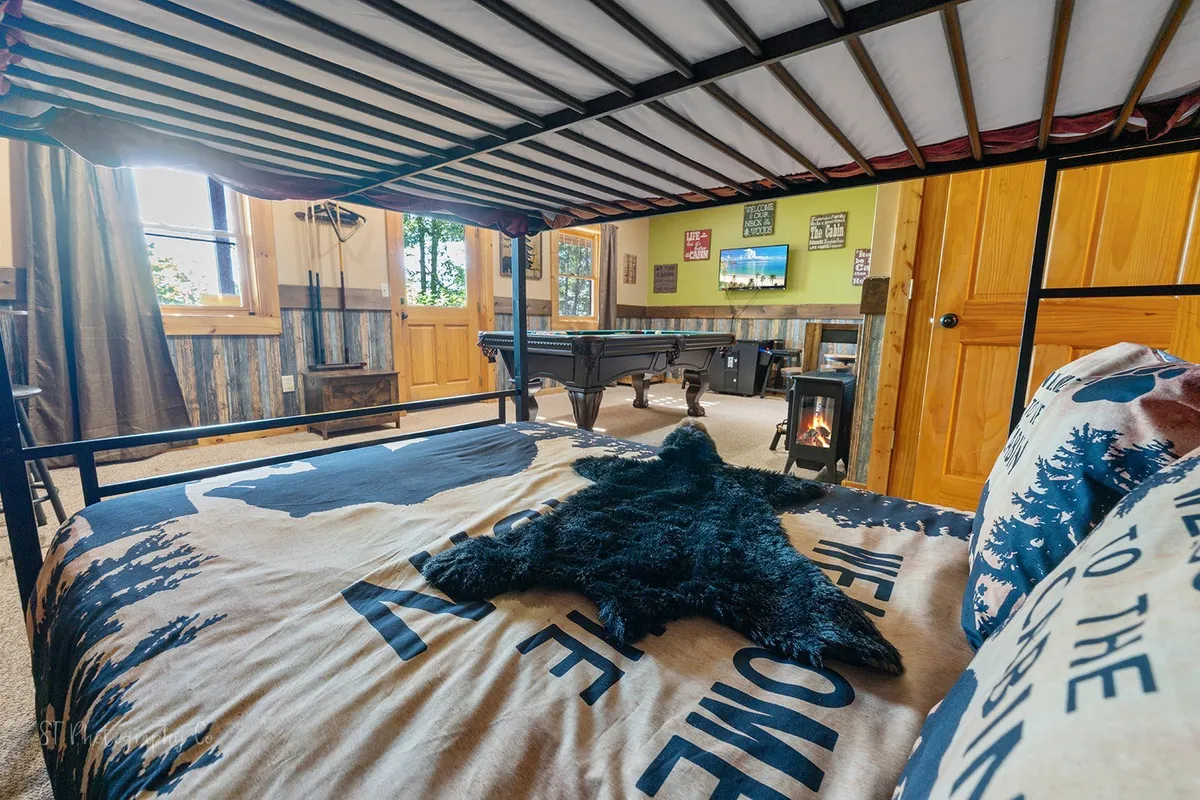 A rustic, comfortable entertainment area featuring a pool table, bear skin rug, TV, and a bunk bed. The space is ideal for late-night games, storytelling, and sleepovers, supporting both play and relaxation after a day of adventure.