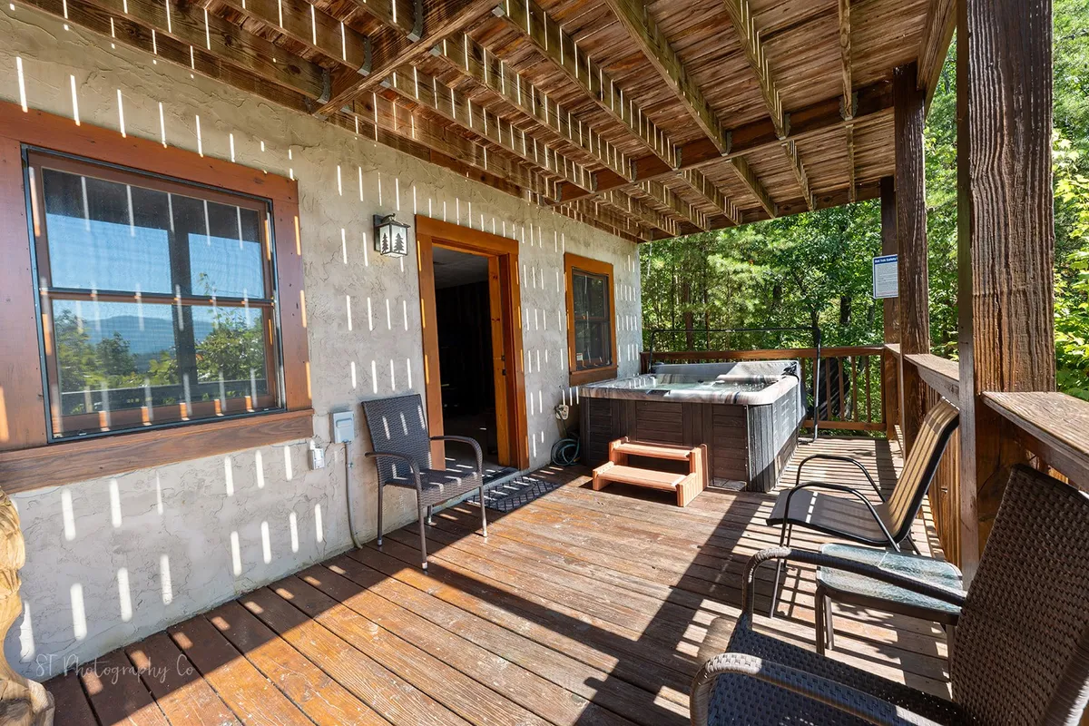 A spacious wooden deck features a hot tub and inviting outdoor seating, framed by tall trees and open skies. The area evokes relaxation, with space for both soaking and lounging, and hints at sunset or starlit evenings.